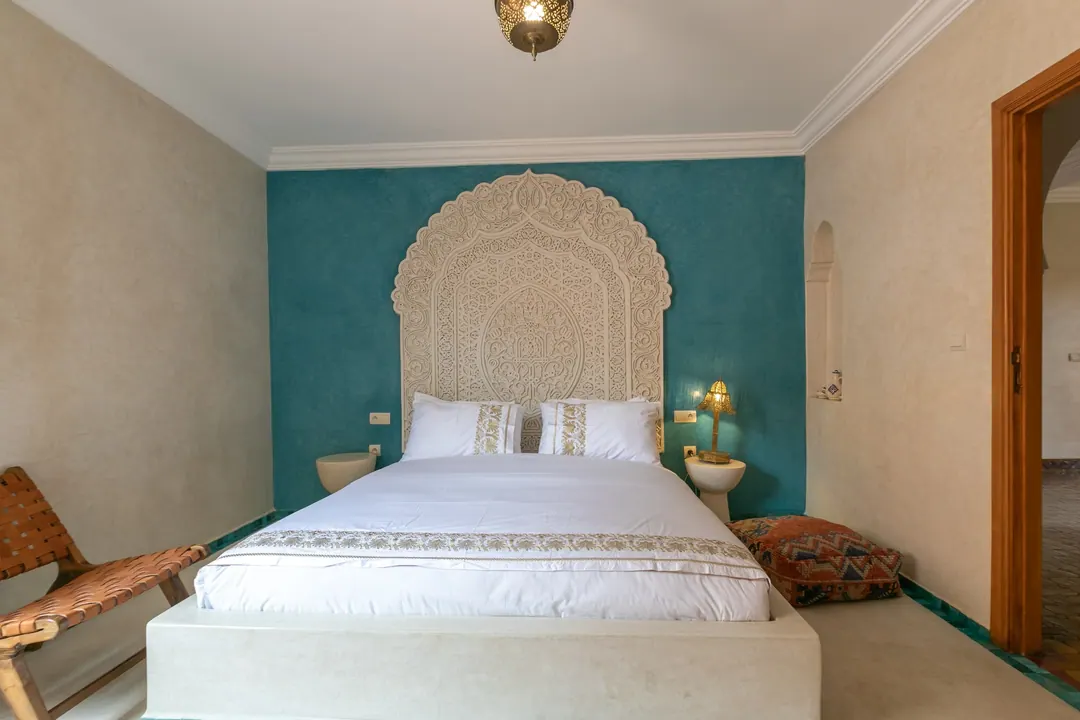 Turquoise room: carved plaster headboard against a deep turquoise wall, leather lounge chair