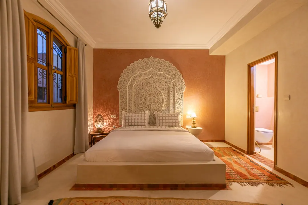 Terracotta room: carved white headboard on a rose-clay wall, cedar shutters and Berber rugs