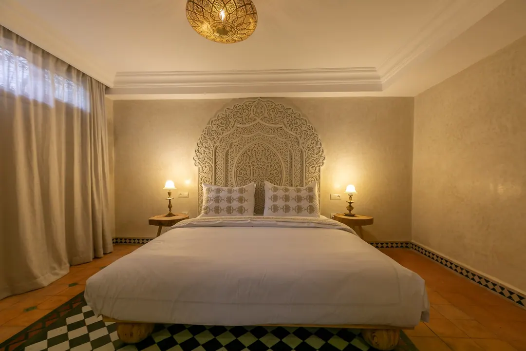 Ivory room: carved plaster headboard, bedside lamps and a black-and-white zellige floor