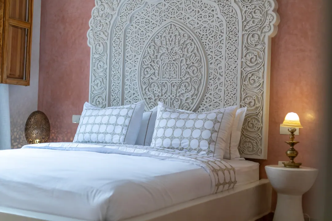 Terracotta room: carved white headboard on a rose-clay wall, cedar shutters and Berber rugs