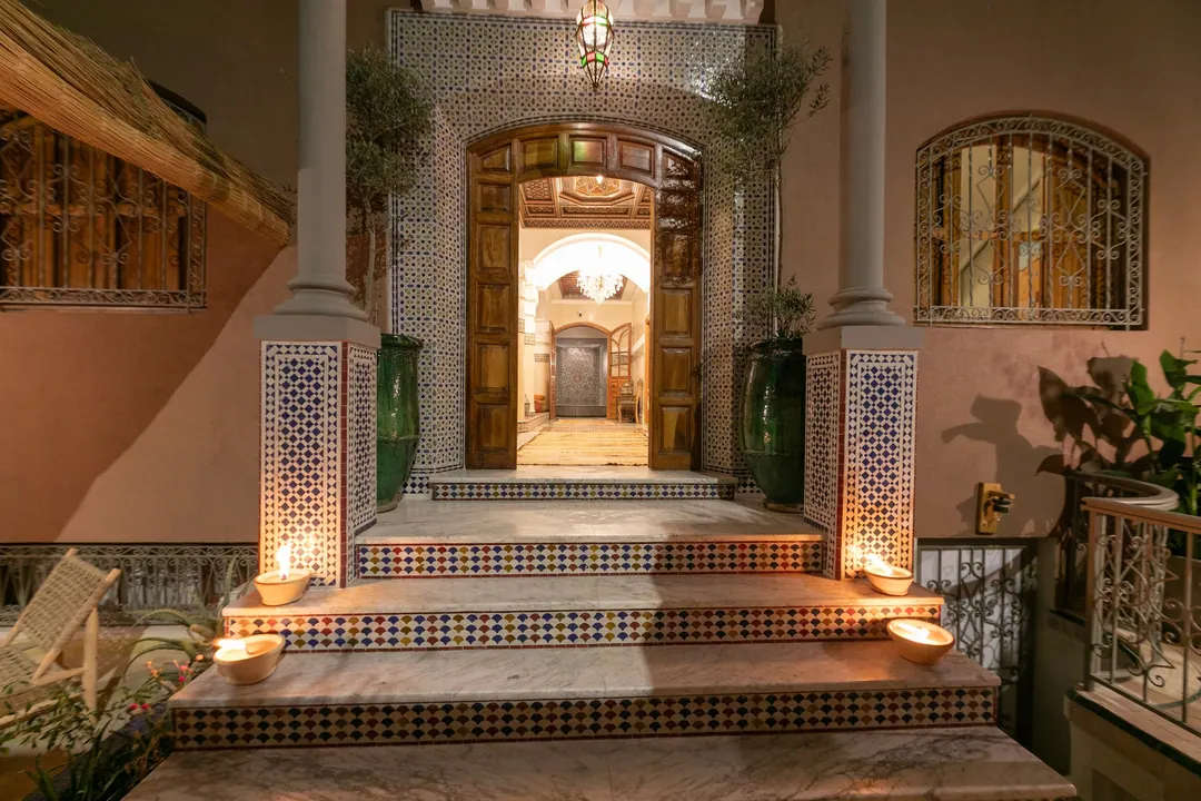 Candle-lit tiled steps leading to the carved wooden door of the riad at night