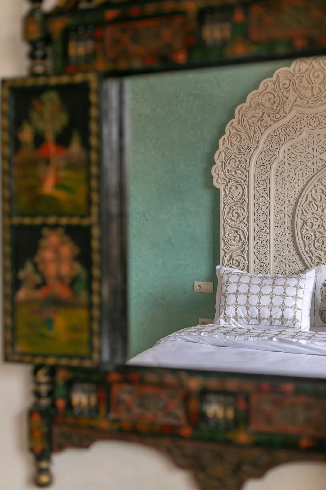Jade room: king bed beneath a carved plaster headboard, pale jade tadelakt walls and Berber rug