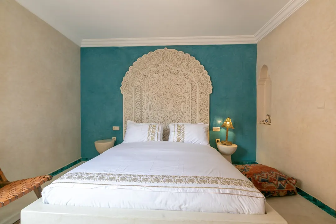 Turquoise room: carved plaster headboard against a deep turquoise wall, leather lounge chair