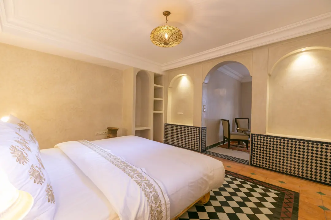 Ivory room: carved plaster headboard, bedside lamps and a black-and-white zellige floor