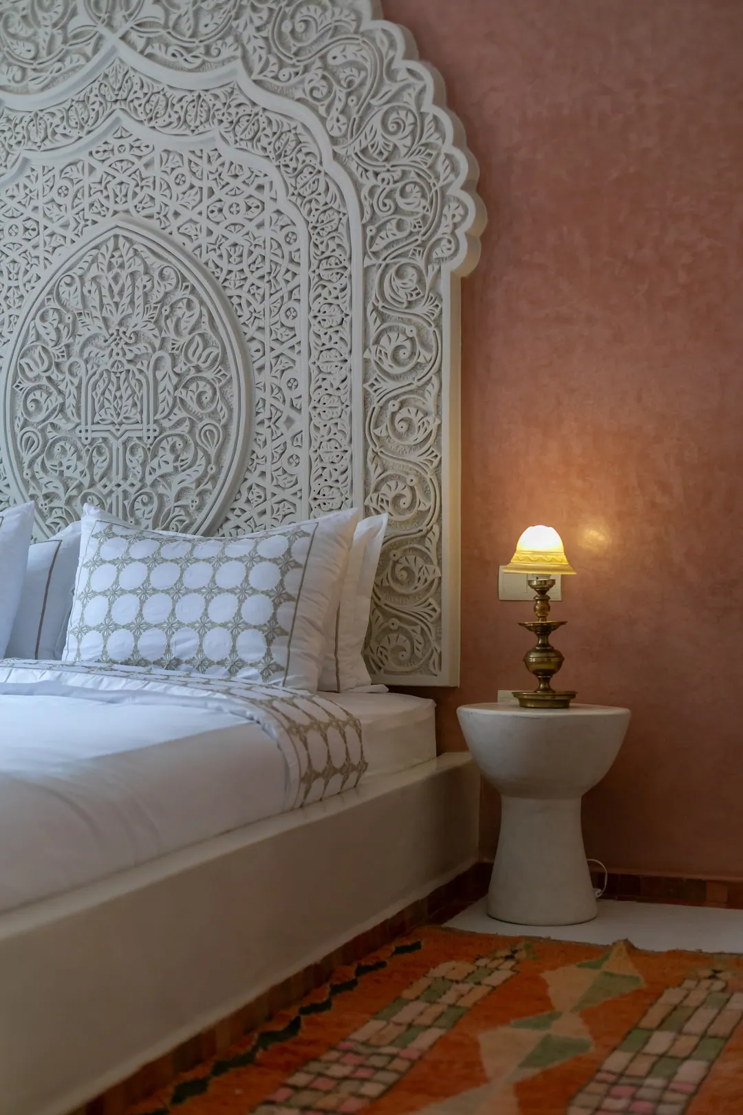 Terracotta room: carved white headboard on a rose-clay wall, cedar shutters and Berber rugs