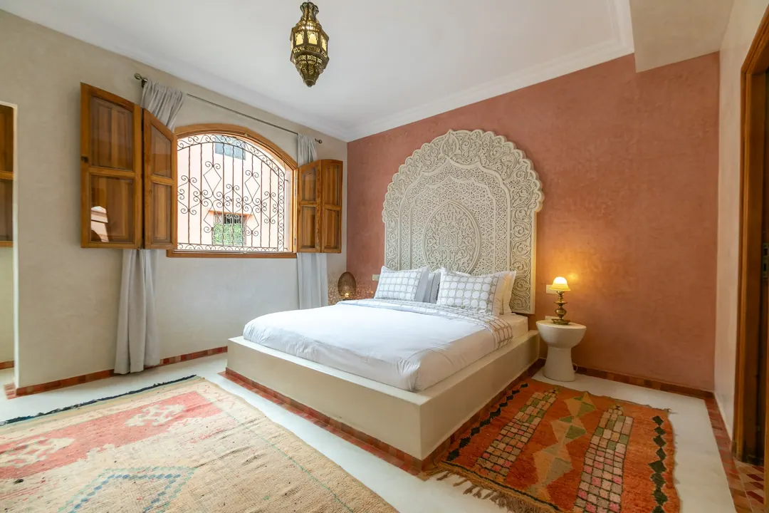 Terracotta room: carved white headboard on a rose-clay wall, cedar shutters and Berber rugs