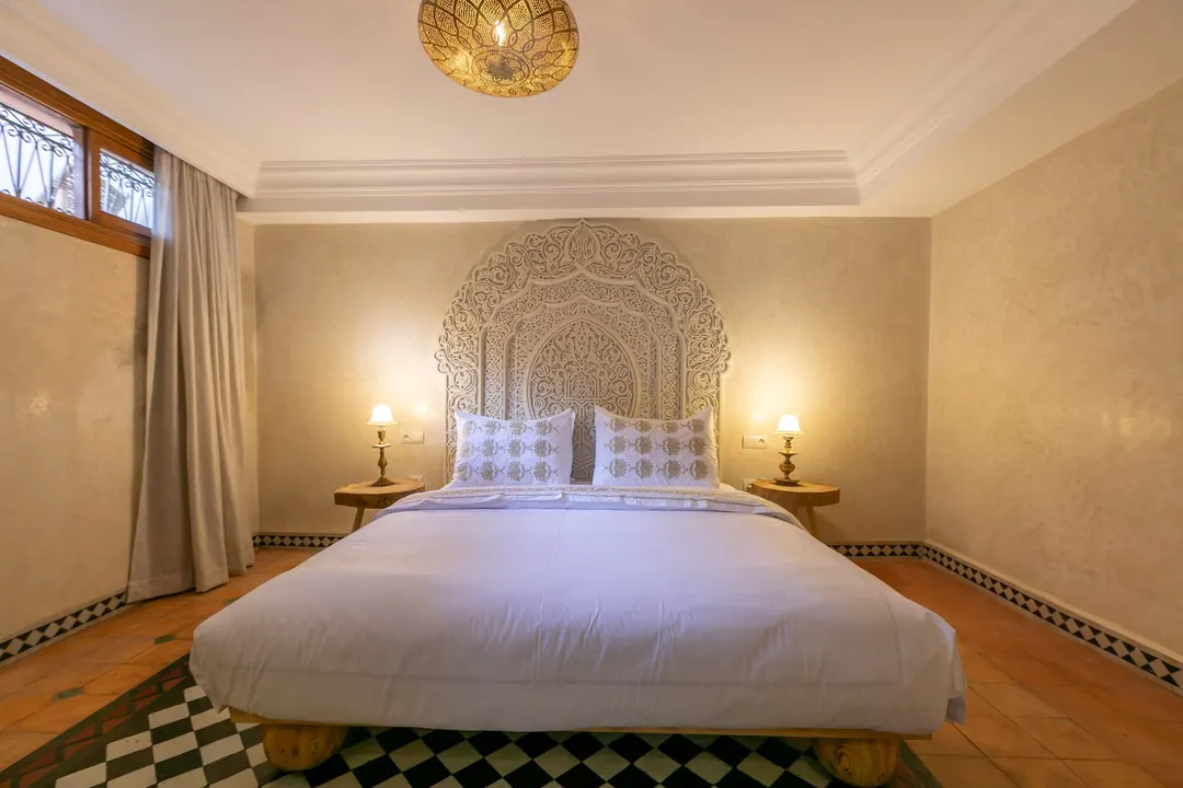 Ivory room: carved plaster headboard, bedside lamps and a black-and-white zellige floor