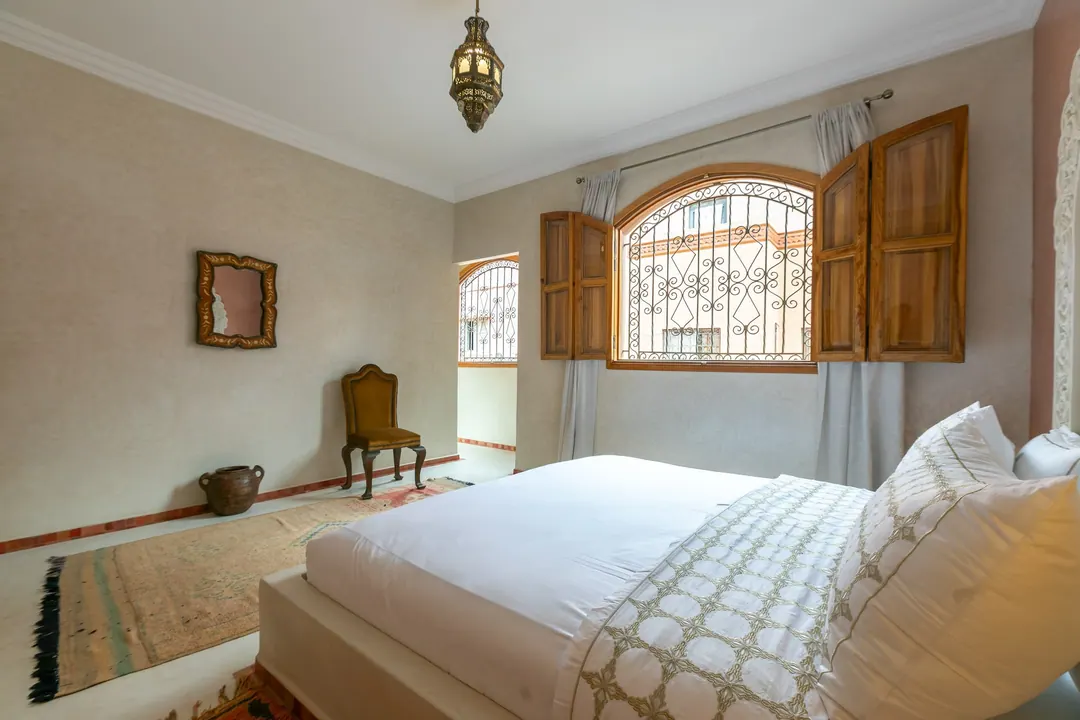 Terracotta room: carved white headboard on a rose-clay wall, cedar shutters and Berber rugs