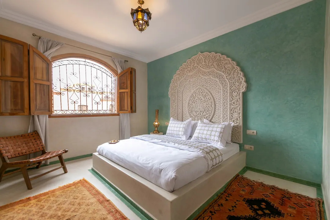 Jade room: king bed beneath a carved plaster headboard, pale jade tadelakt walls and Berber rug