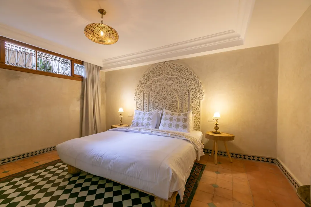 Ivory room: carved plaster headboard, bedside lamps and a black-and-white zellige floor