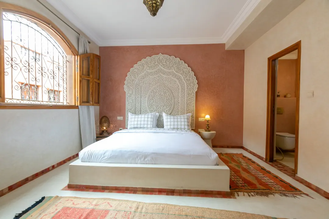 Terracotta room: carved white headboard on a rose-clay wall, cedar shutters and Berber rugs