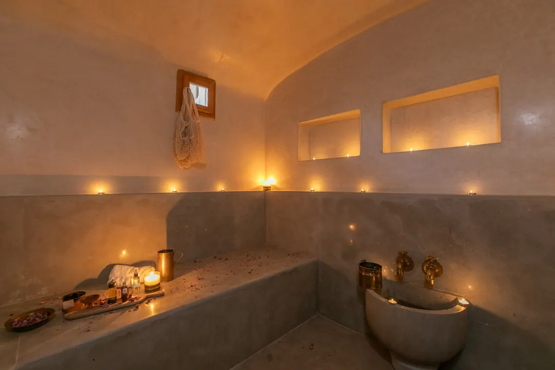 Candle-lit tadelakt hammam with a heated stone bench and copper basin
