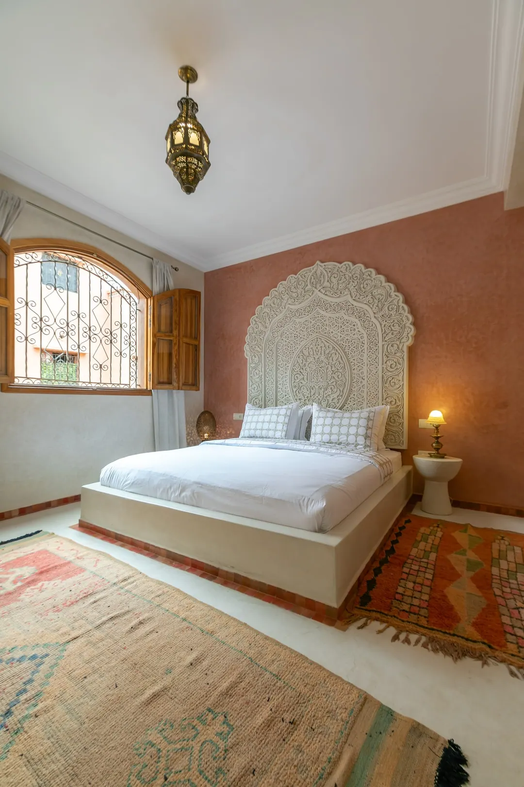 Terracotta room: carved white headboard on a rose-clay wall, cedar shutters and Berber rugs