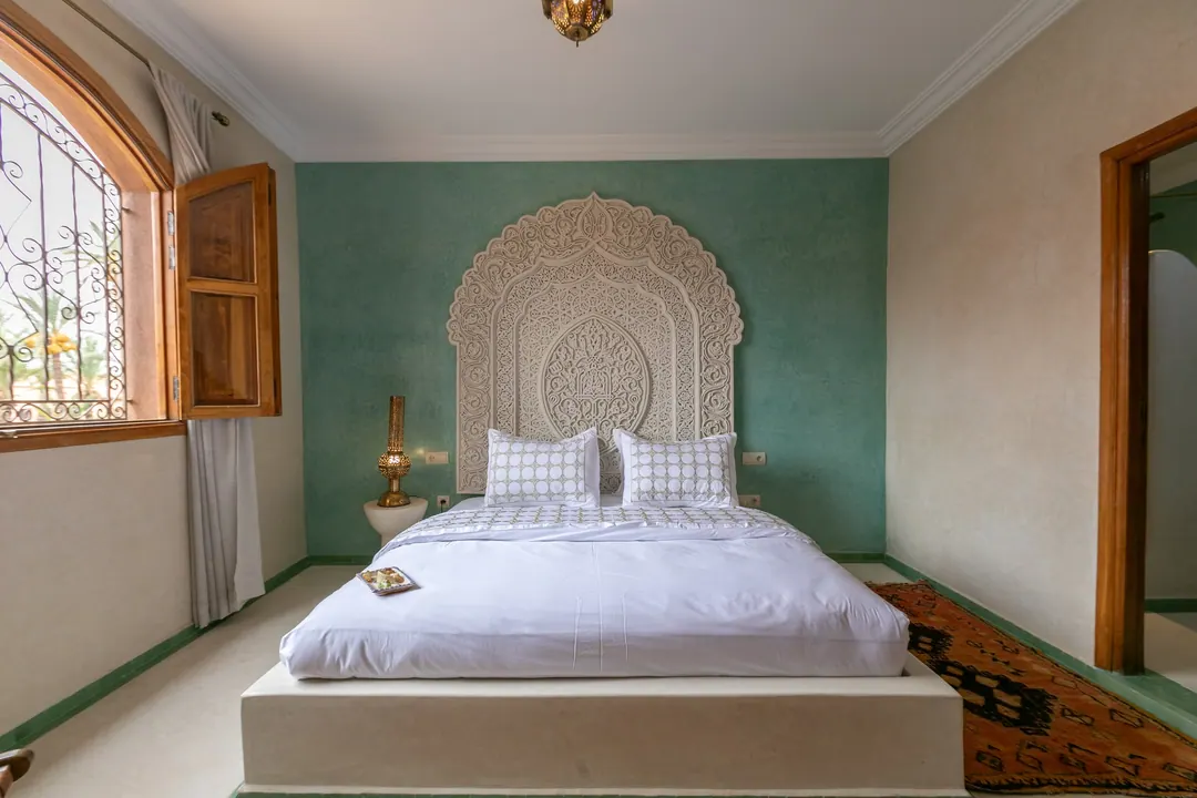 Jade room: king bed beneath a carved plaster headboard, pale jade tadelakt walls and Berber rug