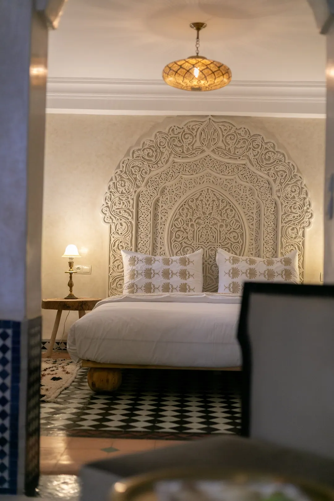 Ivory room: carved plaster headboard, bedside lamps and a black-and-white zellige floor