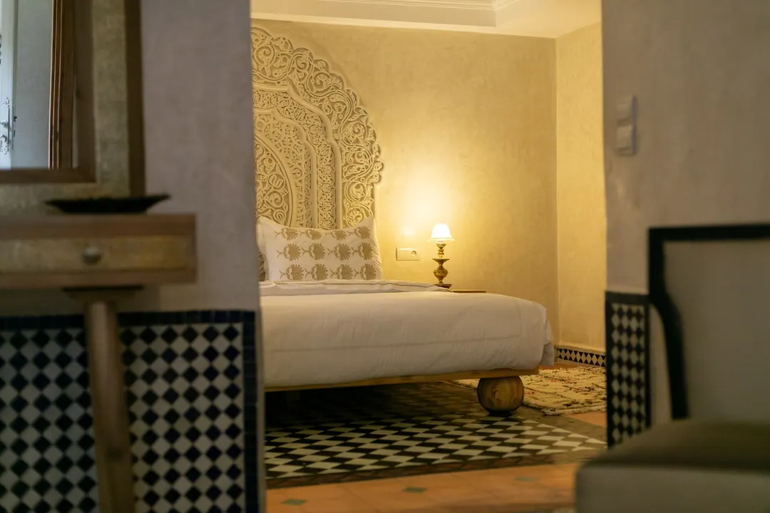 Ivory room: carved plaster headboard, bedside lamps and a black-and-white zellige floor