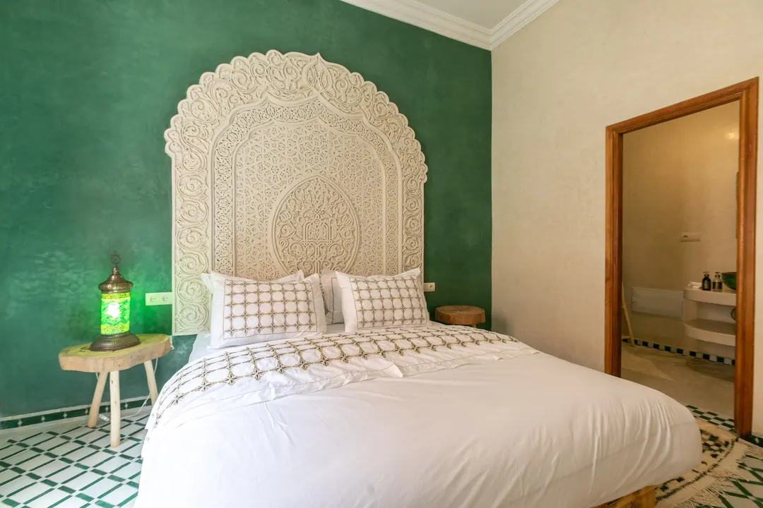 Emerald room: carved headboard on an emerald tadelakt wall, green lantern and zellige floor