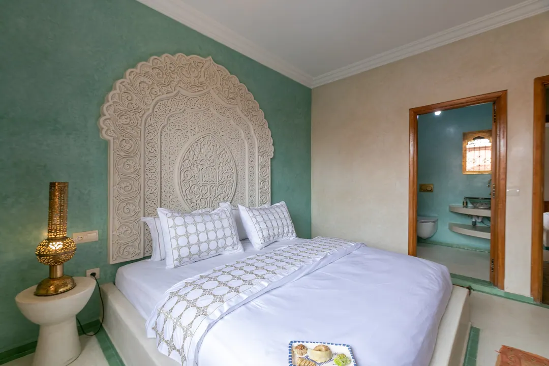 Jade room: king bed beneath a carved plaster headboard, pale jade tadelakt walls and Berber rug
