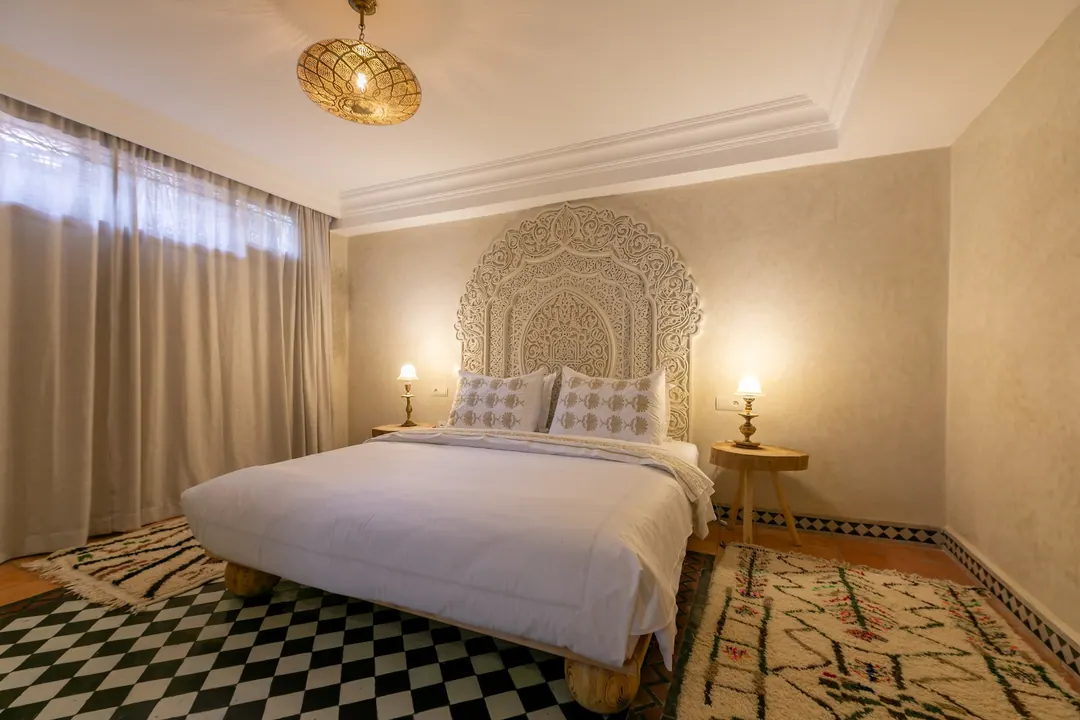 Ivory room: carved plaster headboard, bedside lamps and a black-and-white zellige floor